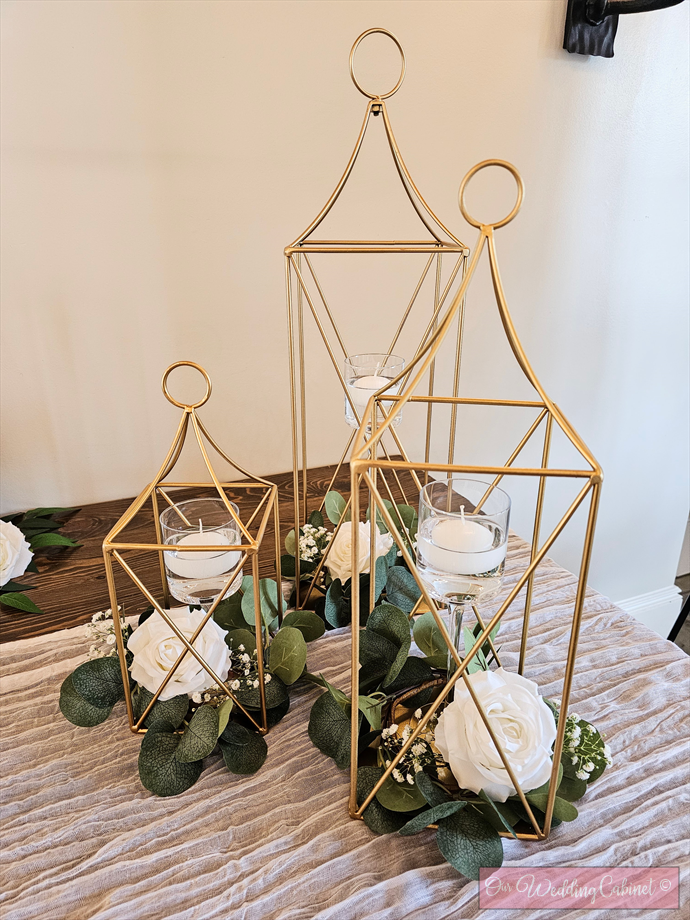 Set of 3 Metal Lanterns, Gold: each set will get a 24",19",13" Lantern with eucalyptus candle rings that will fit glass vases. **VASES WILL NEED TO BE ADDED SEPERATELY, 6.25",7.5",9"**